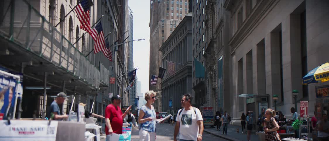 Small group of people holding up signs as others walk by in the middle of the street with buildings holding up flags
