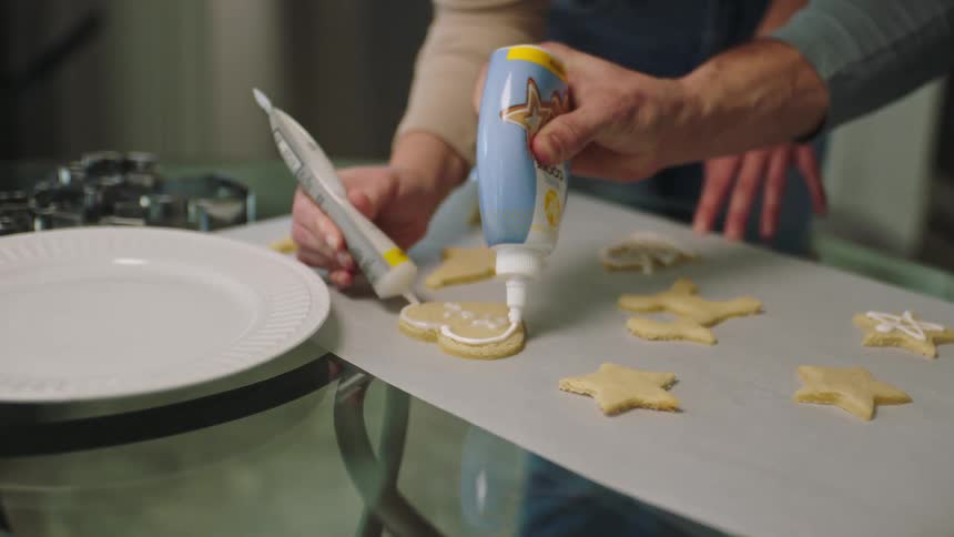 A man and woman are icing cookies