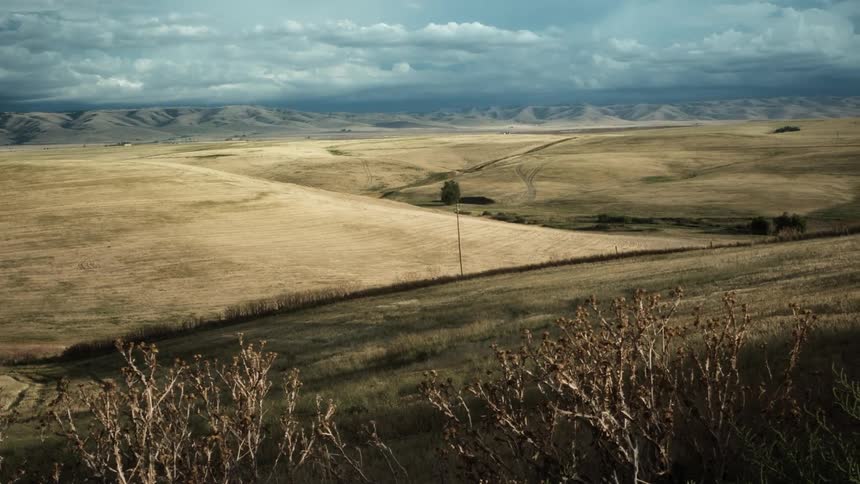 A vast open land with rolling fields and distant mountains