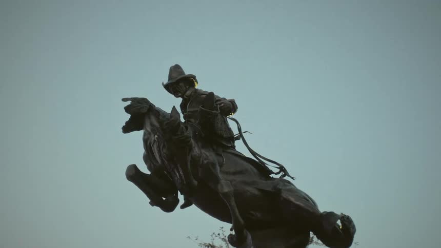 Bronze statue outdoors during day time of a man wearing a hat and riding a horse