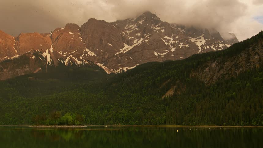 A mountain range with trees and traces of snow sits near a lake