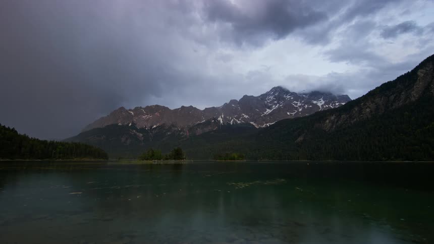 Landscape of snowy mountain ranges with a greenish lake in a cloudy sky