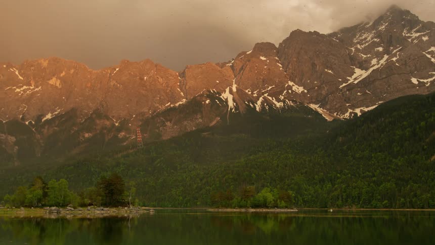 Reflective lake with mountains and greenery around on cloudy day