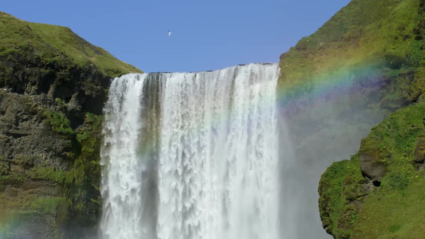 A waterfall on a mountain forms a rainbow during a sunny day