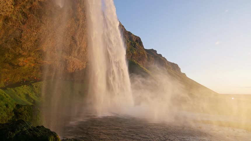 A waterfall flows down a cliff into a calm lake at sunset