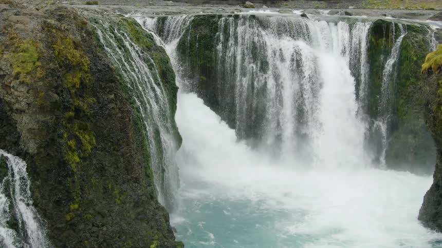 A mountain range has a massive waterfall in the middle of it crashing into the water below