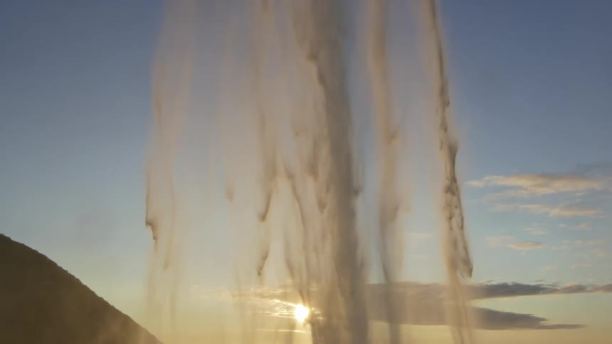 Free falling water in slow motion from a waterfall with sun in a sky with few clouds