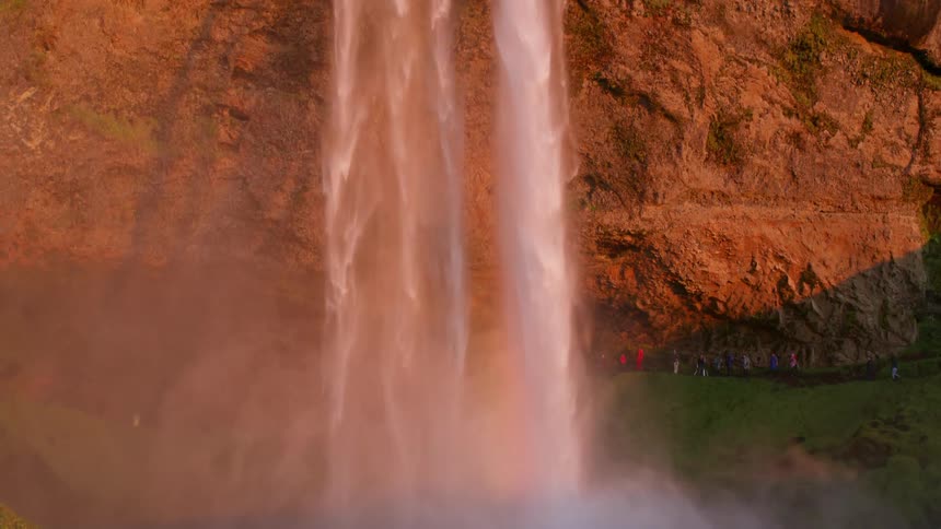 Sightseers stand near base of cliff watching waterfall