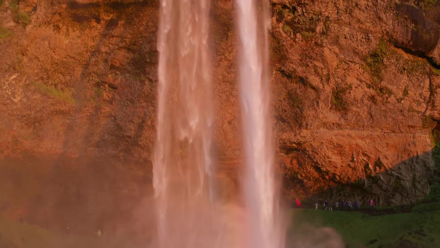 Waterfall outdoors next to a cliff with people watching it during day time