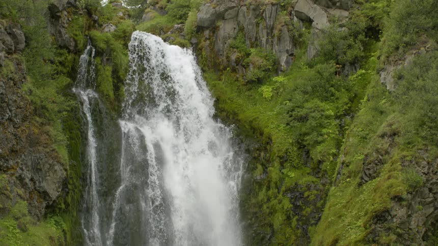 A waterfall with water falling from a slope of rocks full of vegetation