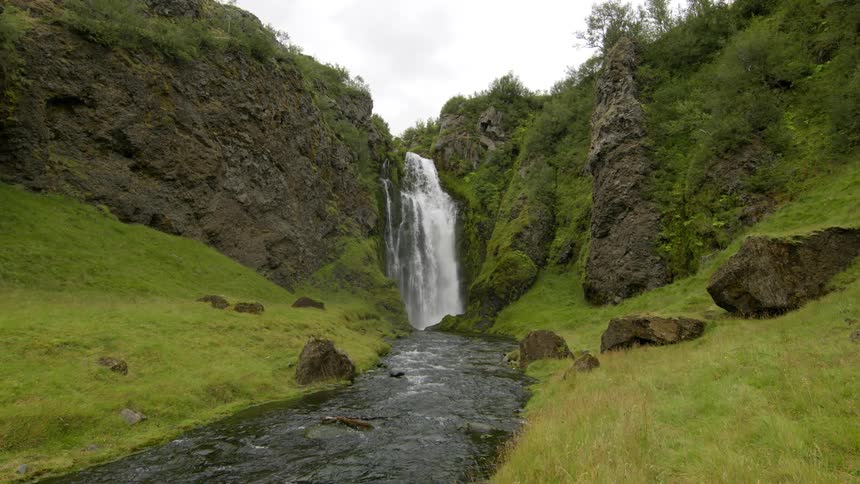 Landscape of a small waterfall giving access to a small flowing river and half mountains