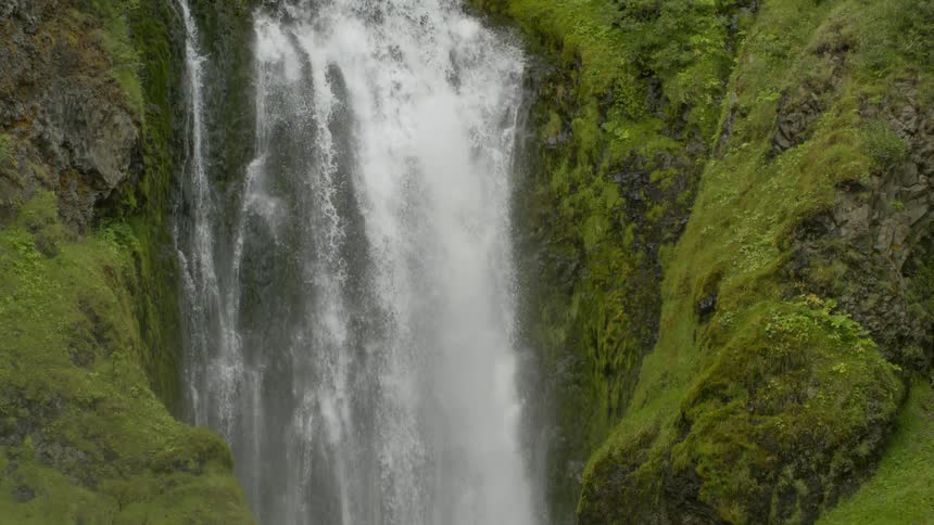 Water landscape of a freefalling waterfall with swirling mountains covered in many