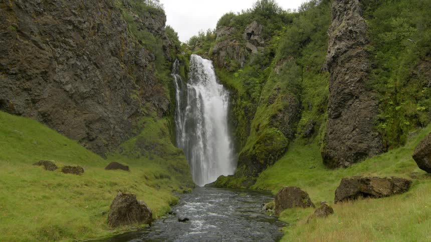 Waterfall cascading in the midst of nature feeding into a river on a cloudy day