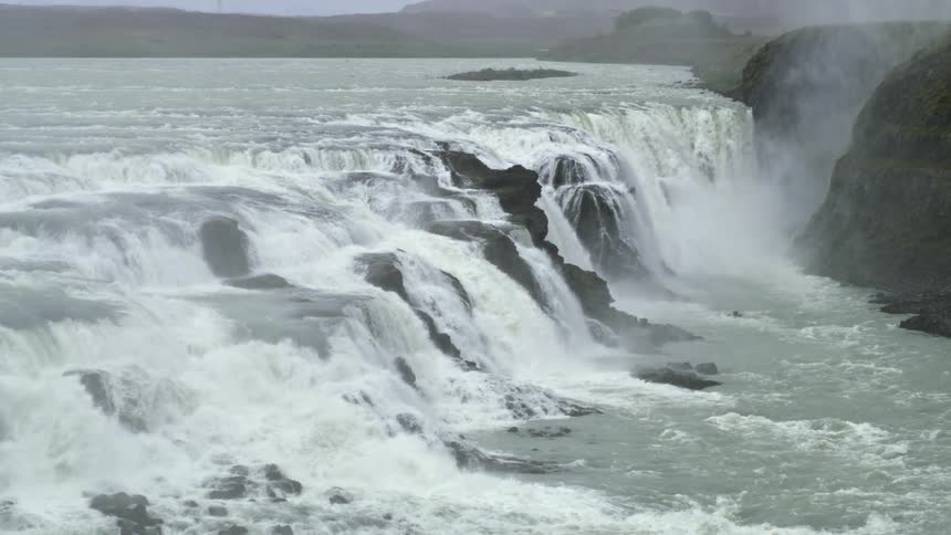 Large waterfall creates mist over nearby mountains as it flows down cliff