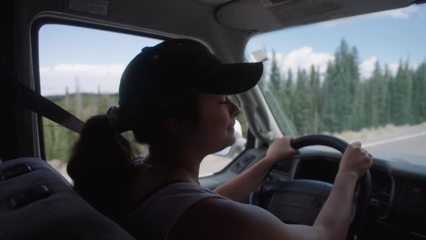 Female driver inside of a car on a road surrounded by trees during day time