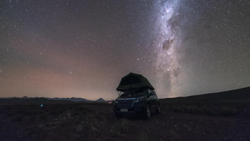 A camper sits by the side of a busy road at night