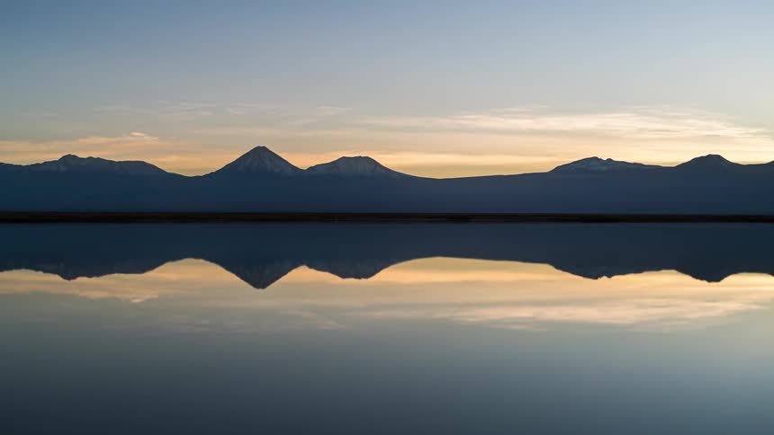 Natural landscape of the day darkening and dawning in timelapse overlooking a reflective lake with mountain ranges in the background