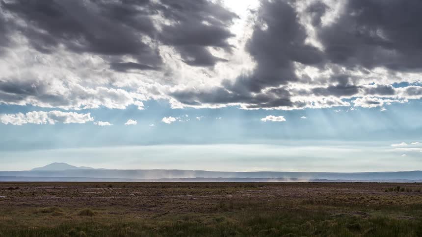 A grassy field with the sun hidden behind the clouds