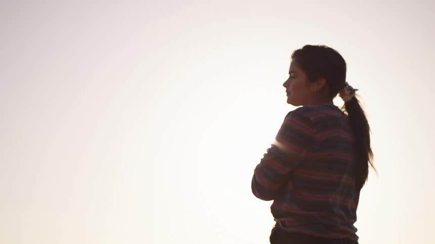 Sun shines brightly onto woman standing alone outdoors on a sunny day