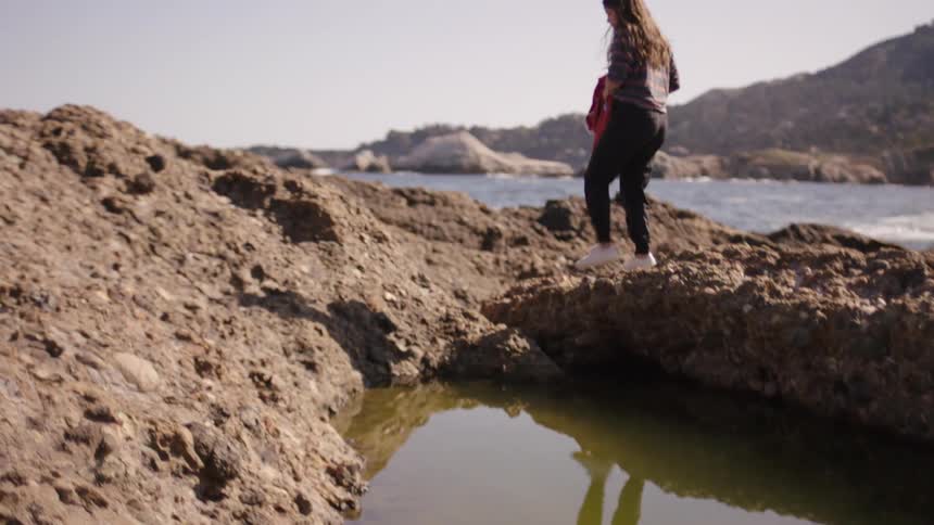 A woman walking on the rocks at the beach during the day
