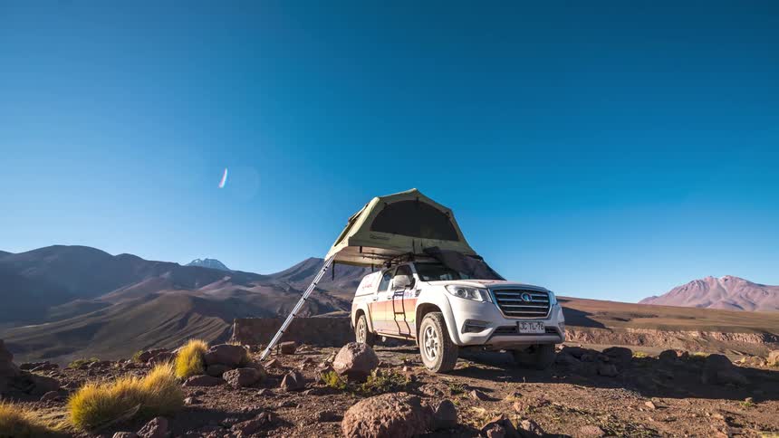 Ladder leads to tent set on roof of vehicle parked in rough arid terrain