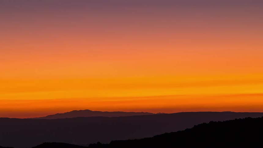Silhouette and landscape of mountains with orange dusk sky with the sun setting in timelapse