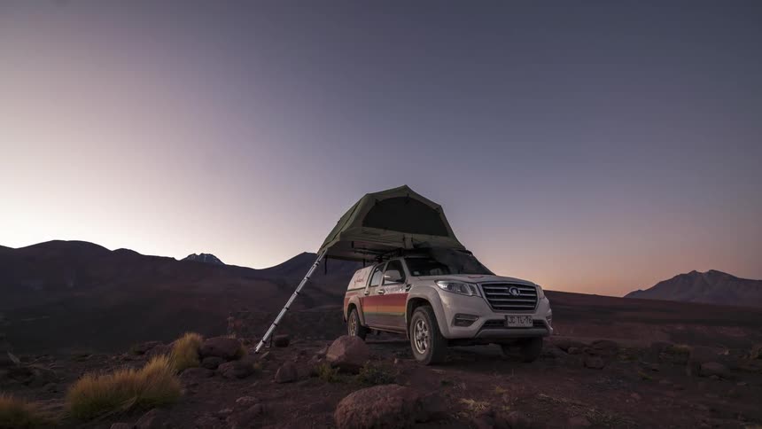 Vehicle with a rooftop tent amidst mountains with the day transitioning from dusk to dawn in timelapse