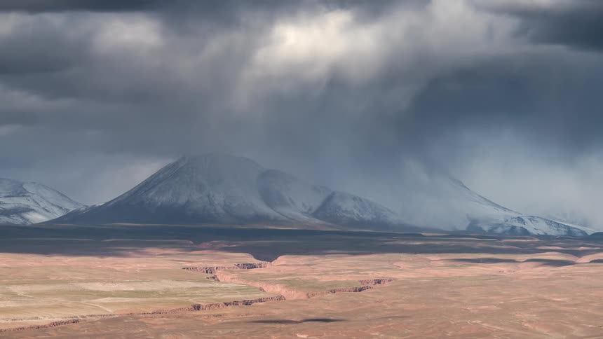 Landscape with desertlike terrain and in the background a snowcovered mountain under a cloudfilled sky in timelapse