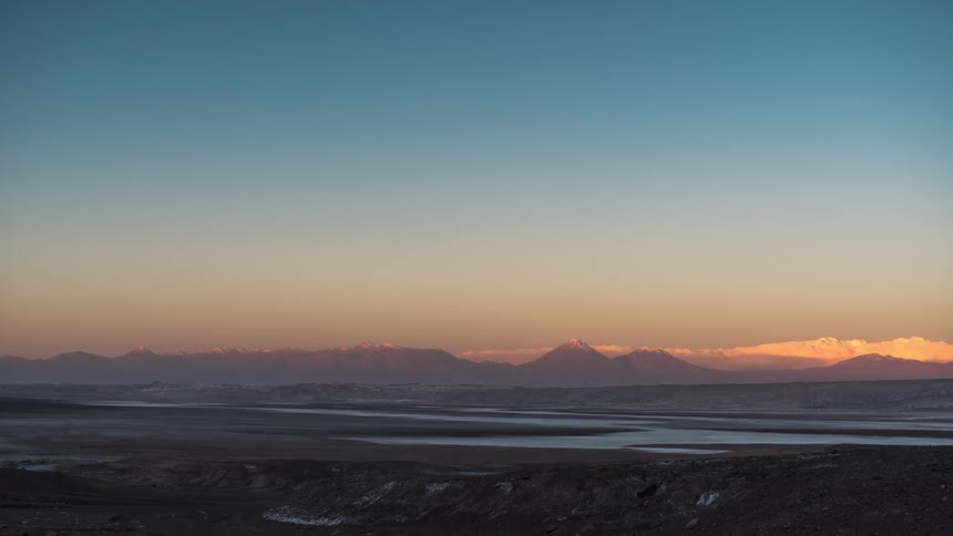 Natural landscape of a lake surrounded by a mountain range with the day transitioning into night in timelapse