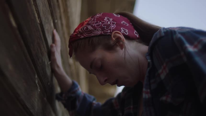 Ill woman leans against exterior house wall while she coughs