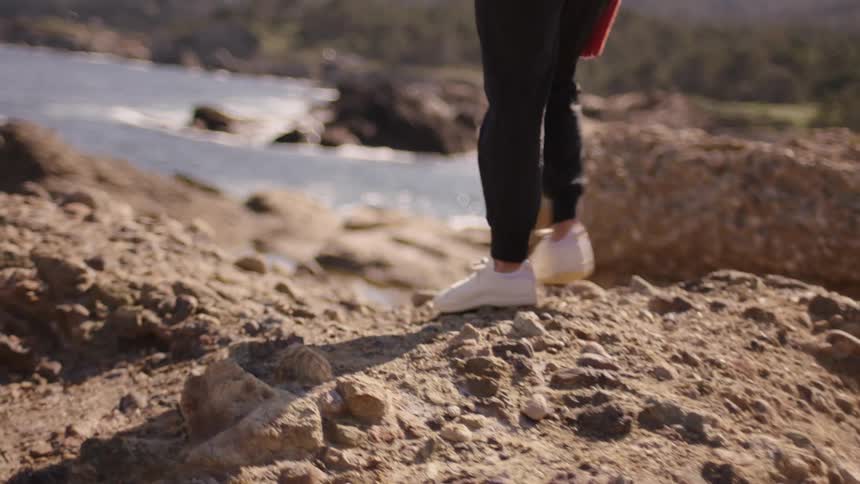 Closeup of a womans legs walking on rocks by the sea
