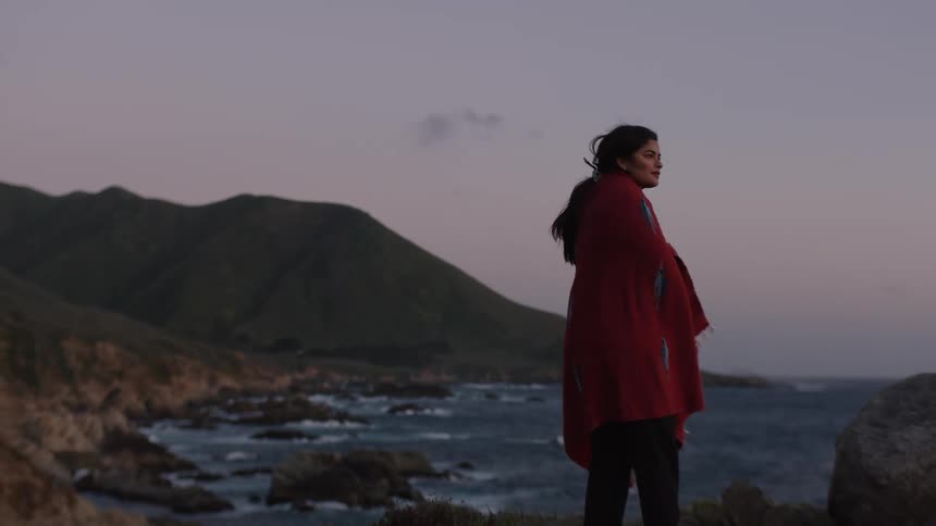Woman with a blanket on the coast facing the sea with a morning sky