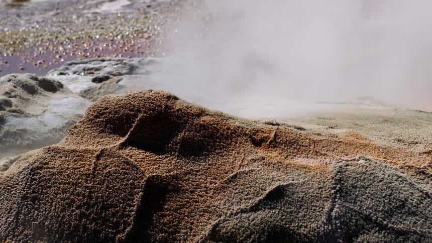 Smoke rising from a rocky ground and a pool of water behind