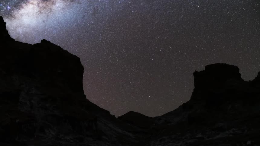 Rock formations in a desert go from bright sunlight to night under a starry sky
