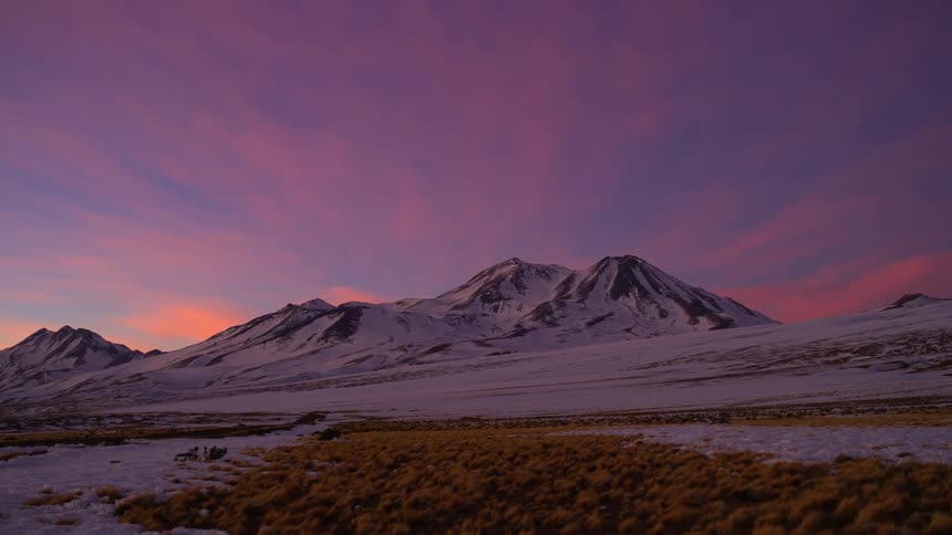 The sun is rising on the snow filled mountains