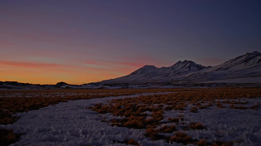 The sun starts to rise over snowy mountains and a canyon