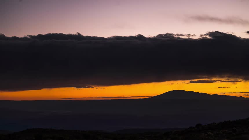 A region with a mountain on the horizon has a sky full of clouds and it is dusk and the sky turns orange