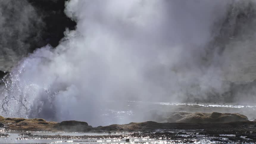 Geyser surrounded by muddy ground releases liquid and vapor into the air