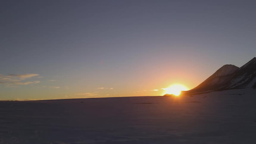 Landscape of snowy ground and mountains with the sun rising on the horizon in timelapse