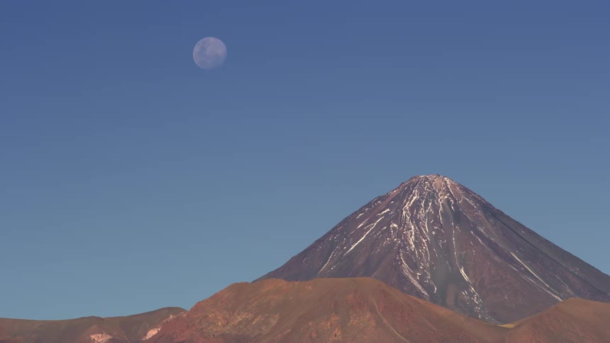 Full moon over a volcanic mountain with snow at the peak