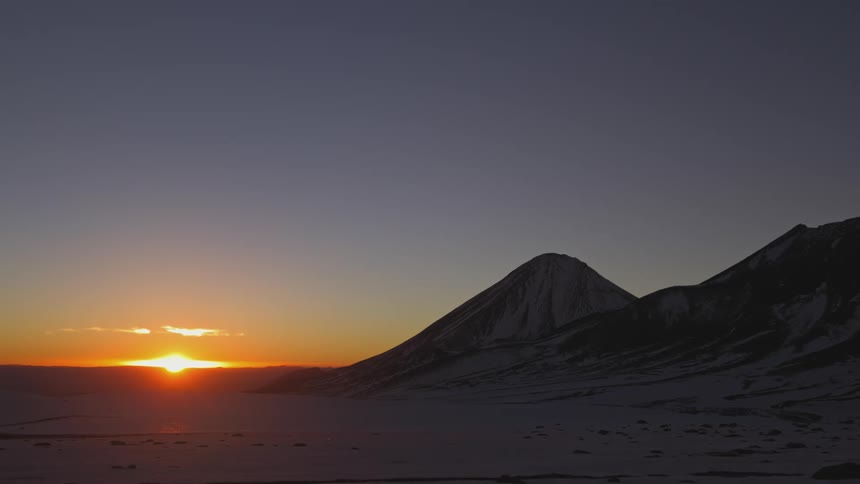 The sun rising over the horizon in a desert region with mountains