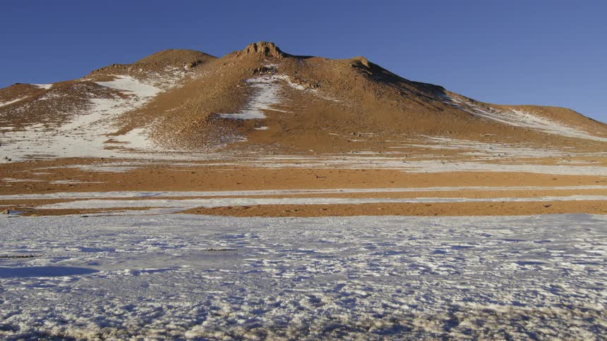 A large mountain illuminated by sunlight and in front the ground is covered in snow