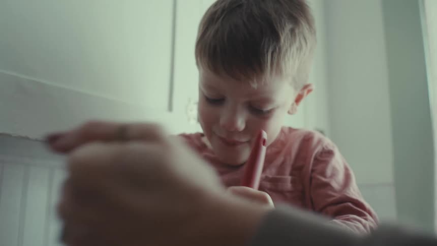 Portrait of a young boy sitting on the counter and with a spatula helping his mother make dough