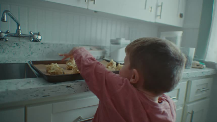 An adult gives food to a child who puts it on a baking tray