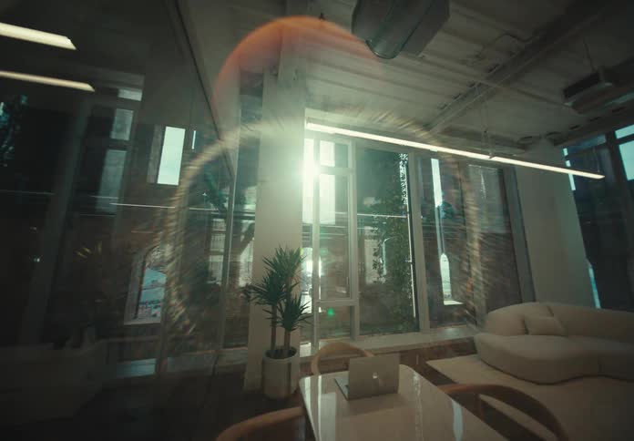 The interior of a room is decorated with glass and reflective furniture while sunlight passes through the window