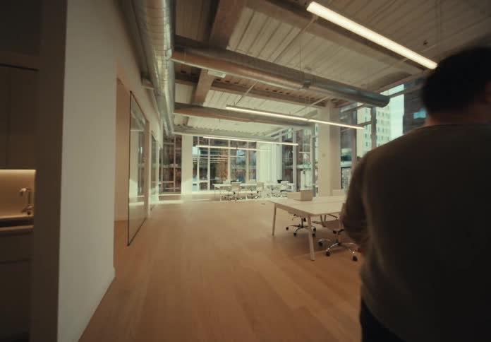A person with his back is walking and goes to the right and an office full of chairs and a white table with a computer on top appears