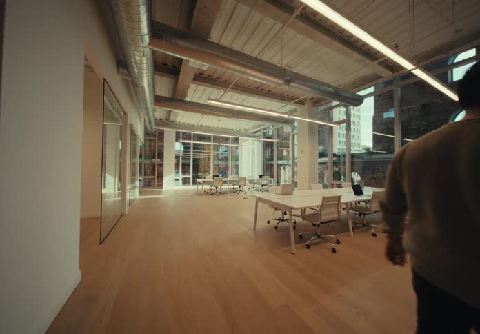 Man wearing a sweater and pants walks into spacious office with white desks and chairs