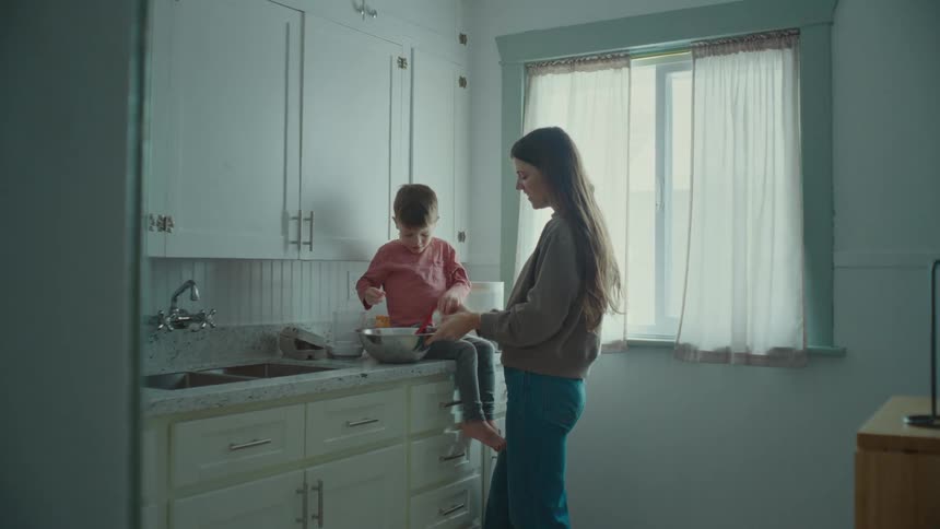 Mother and son in the kitchen preparing food and breaking eggs into a metal bowl
