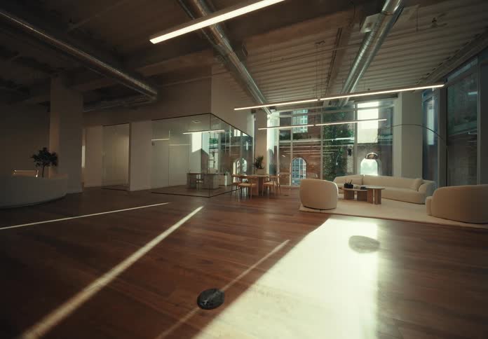 A room with a wooden floor being illuminated by sunlight coming from the glass window and there is some furniture in the room