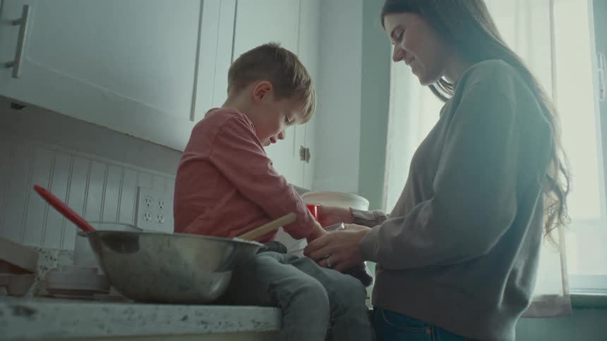 A young mother and son eat chocolate chips together while making Cookies